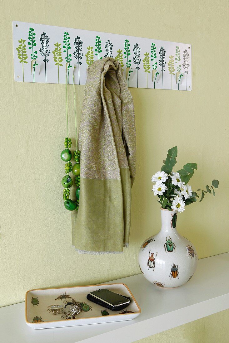 Beetle-patterned key tray and vase in green cloakroom with floral coat rack