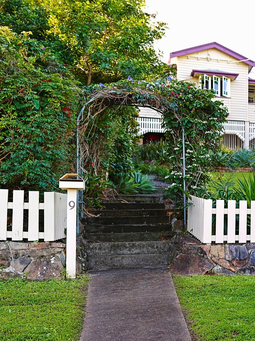 Rosenbogen über Gartentreppe und weisser Lattenzaun vor Landhaus im Queenslander-Stil