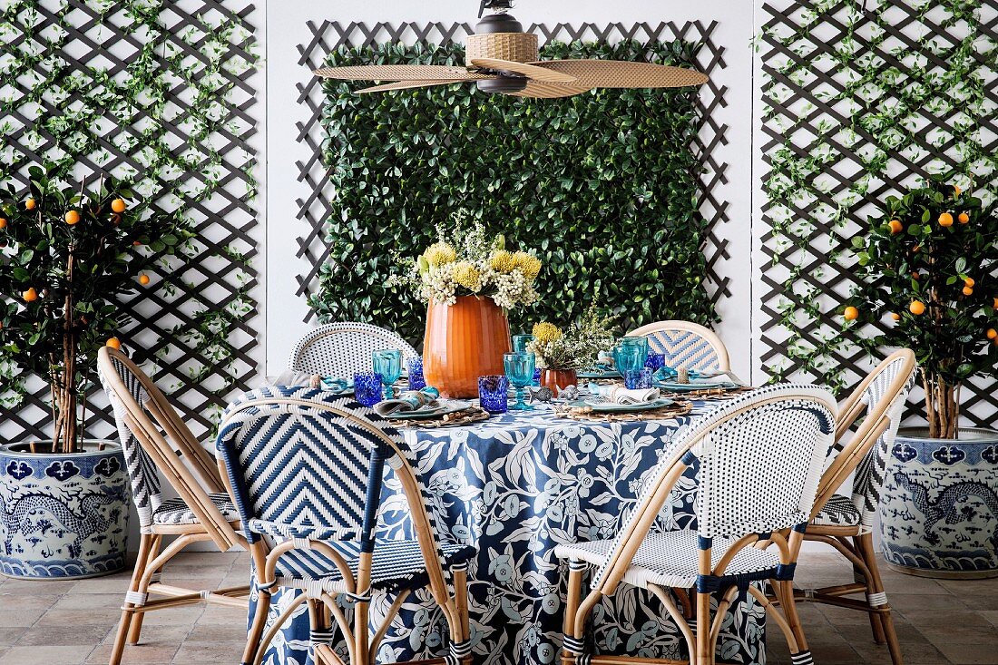 Korbstühle um gedeckten Tisch mit floral gemusterter, blau-weißer Tischdecke unter Deckenventilator