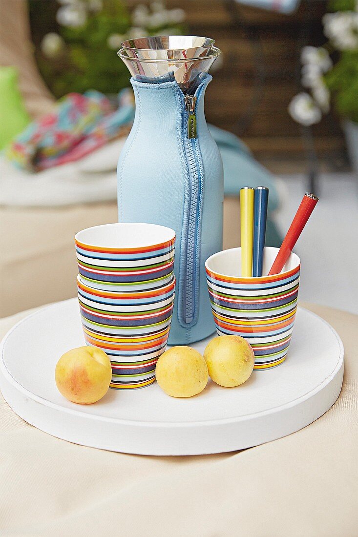 Striped cups, a Thermos flask and yellow plums on a white tray