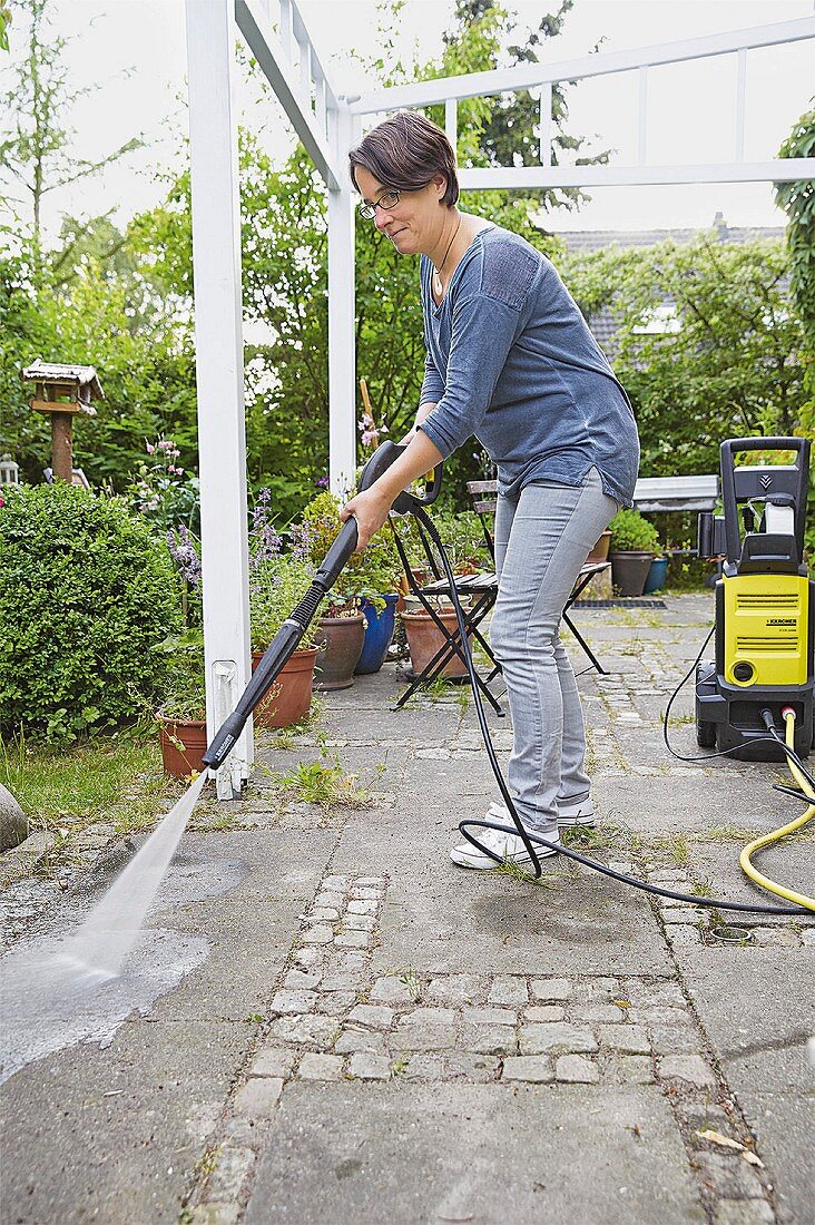 A woman cleaning a terrace with a high pressure cleaner