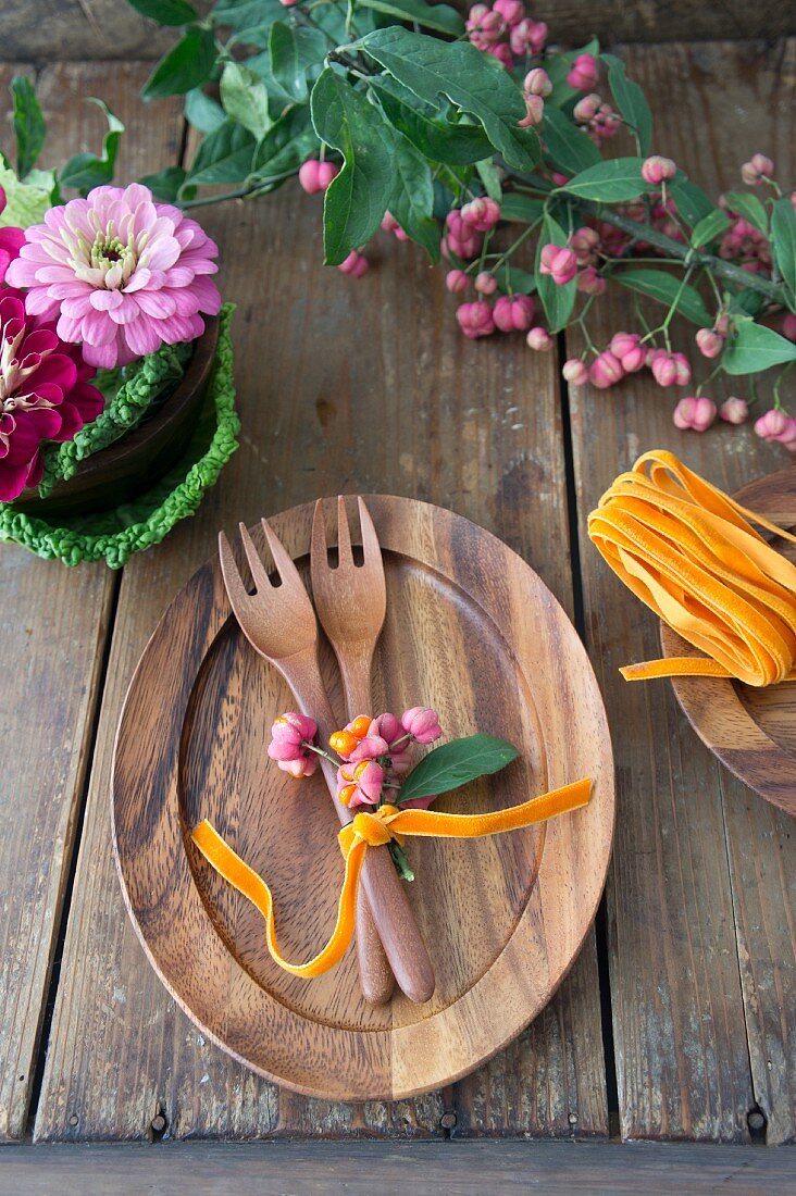 Wooden cutlery on wooden plate decorated with spindle seed pods next to bowl of Savoy cabbage leaves and zinnias