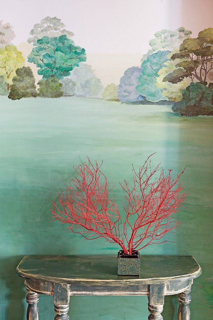 Red-painted branches on console table against mural of green landscape