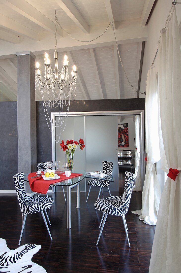 Modern chairs with zebra-patterned covers around glass table in open-plan living area