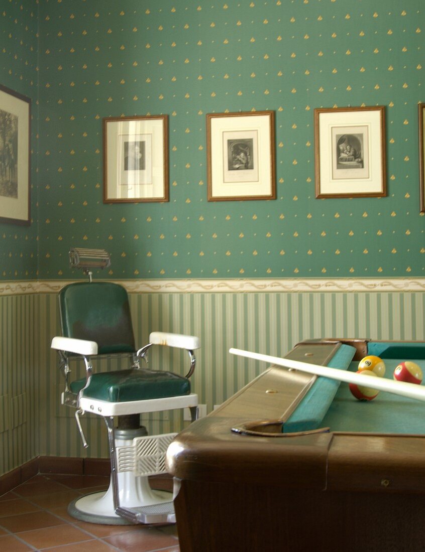 Alter Friseurstuhl und Billardtisch vor klassischer, dreiteilig tapezierter Wand