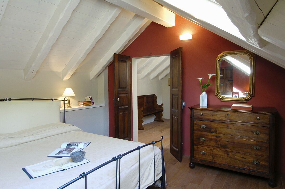 Schlafzimmer unter dem Dach mit antiker Kommode und roter Wand