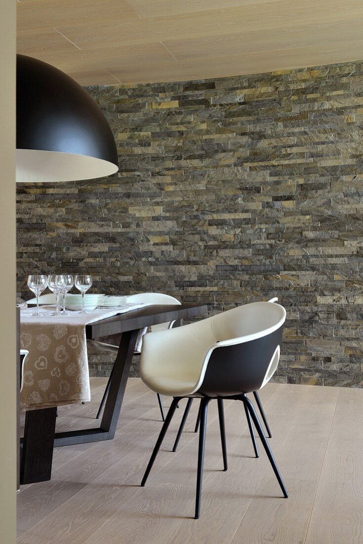Black and white shell chairs and table in dining area with stone wall