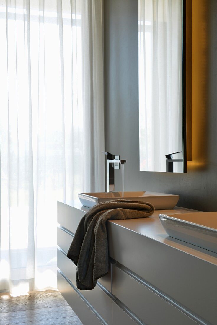 Massgefertigtes Waschtischmöbel vor Spiegel mit integrierter Beleuchtung in elegantem Designerbad