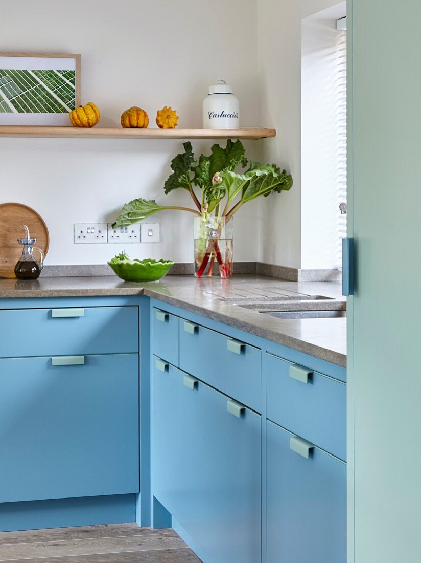 Pale blue, L-shaped kitchen counter with stone worksurface