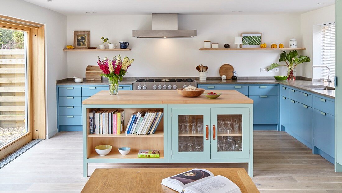 Kücheninsel mit teilweise geschlossenen Unterschränken, im Hintergrund hellblaue Küchenzeile übereck