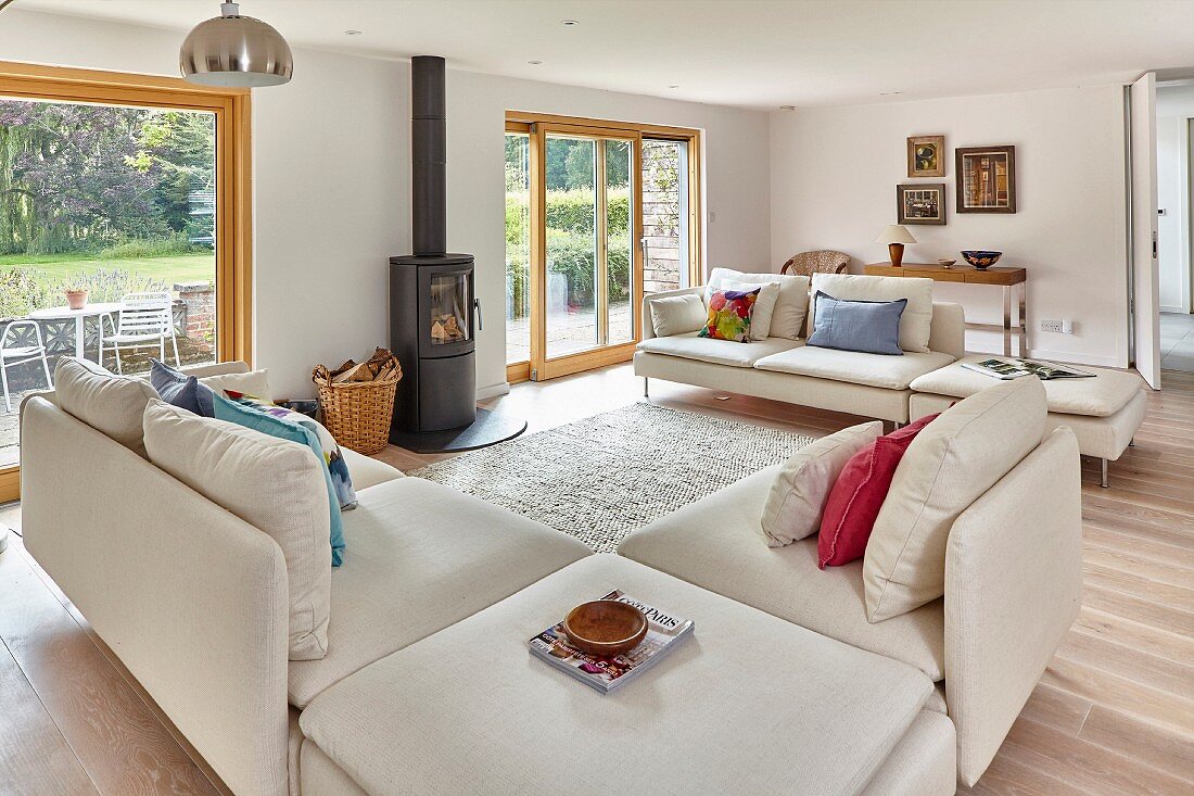 Pale sofa set and log-burning stove between terrace doors in spacious living room