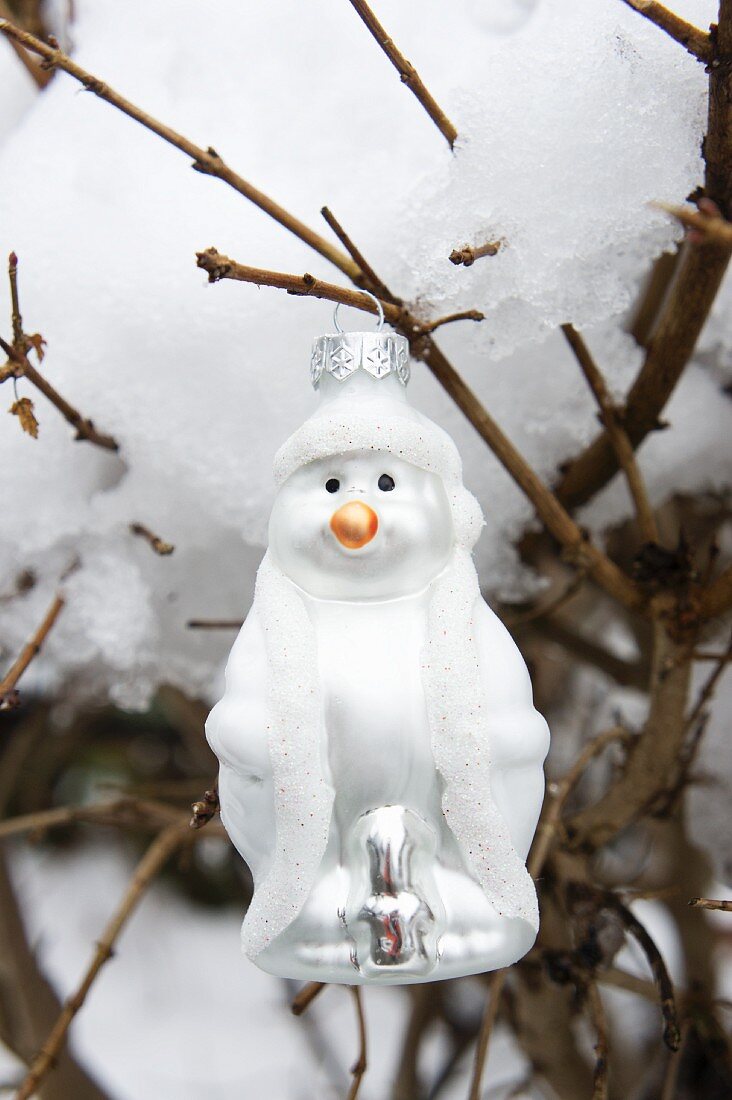 Snowman bauble hung from snow-covered branch in garden