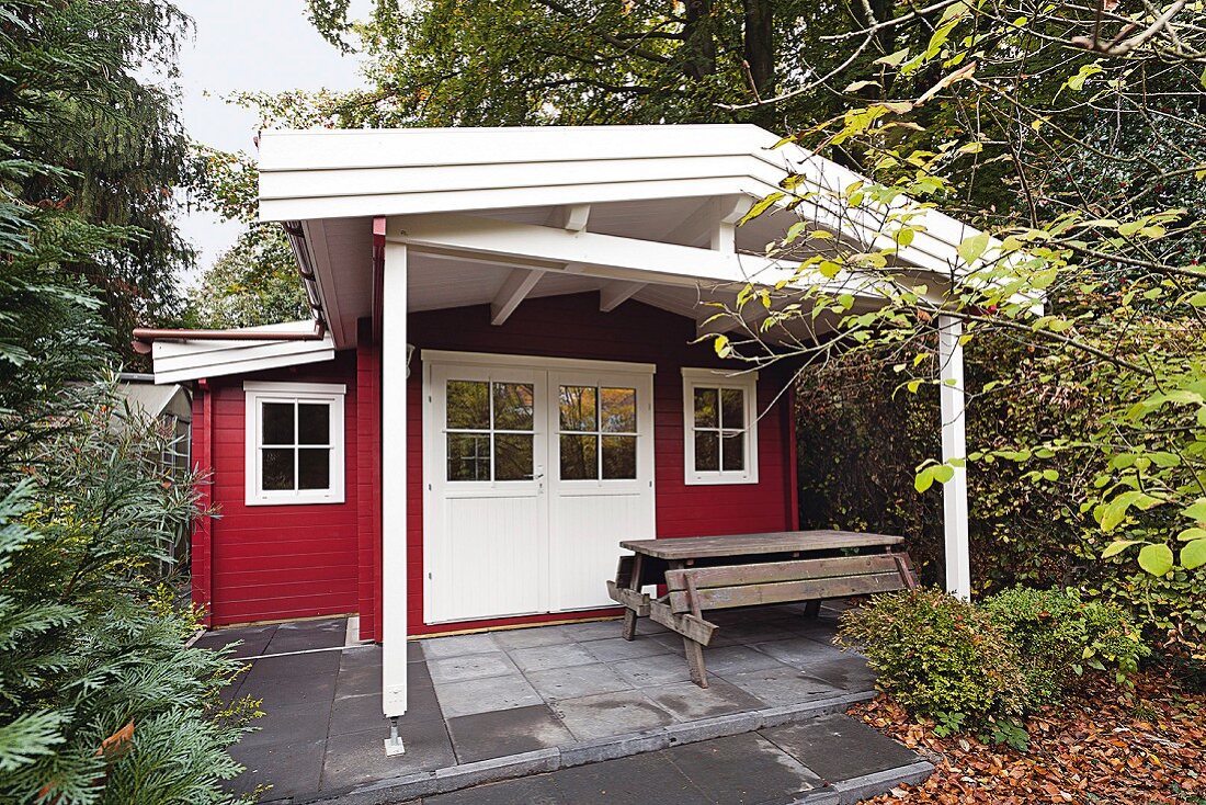 Rot-weisses selbst gebautes Gartenhäuschen mit überdachter Terrasse und Tisch-Bank-Kombination