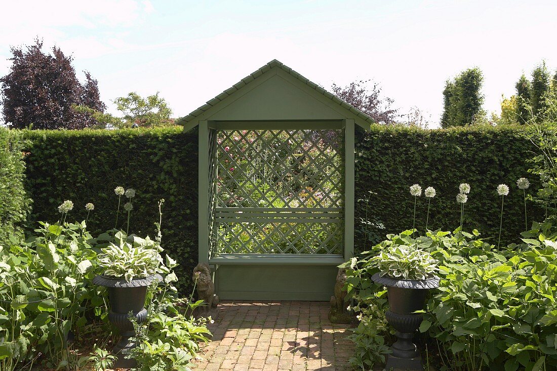 Small arbour with diagonal trellis and tall box hedges bordering summer garden