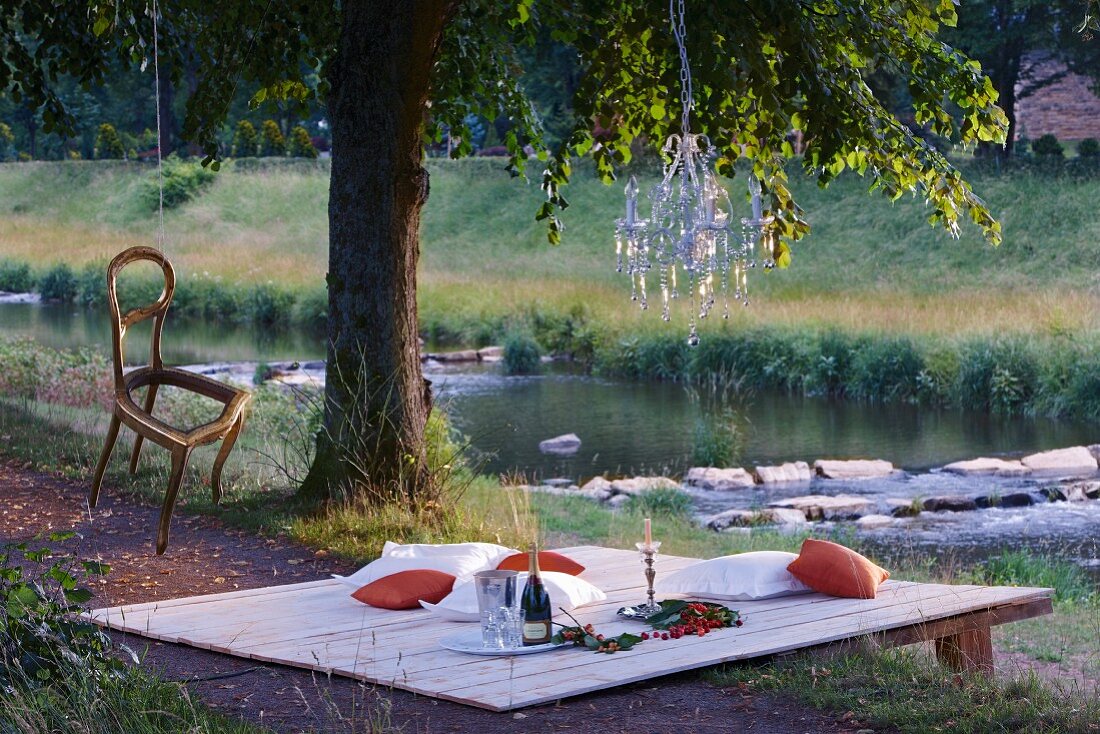 Picknick am Fluss mit im Baum aufgehängten Kronleuchter und Stuhl als Dekoration