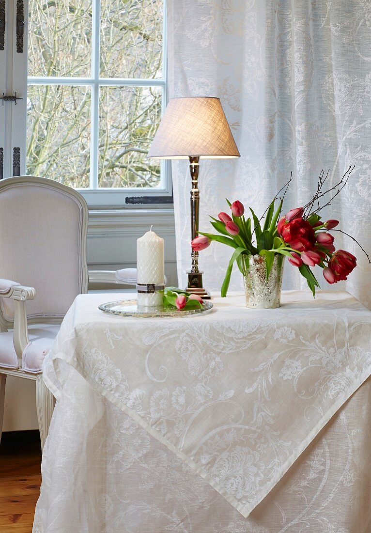 Tisch mit weisser Damasttischdecke, Tischleuchte und Tulpenstrauss