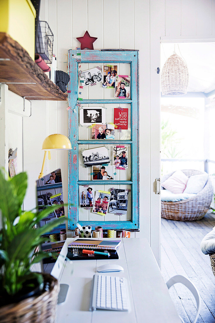 White desk with keyboard and screen, light blue vintage window sash on the side as a pin board for family photos