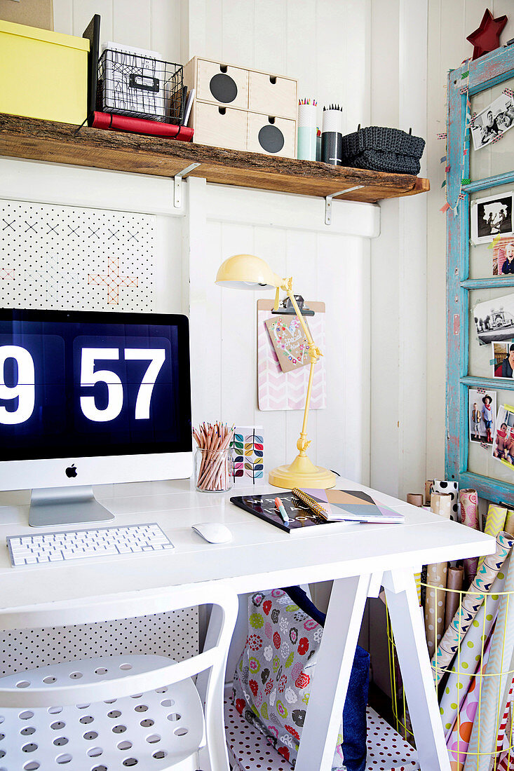 Weißer Schreibtisch mit Computerbildschirm und rustikalem Wandboard neben hellblauem Vintage-Fensterflügel als Pinnwand