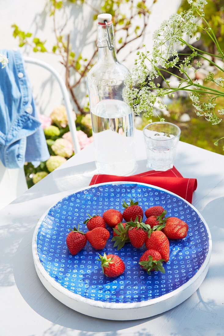 Eine blaue Schale mit frischen Erdbeeren auf dem Gartentisch