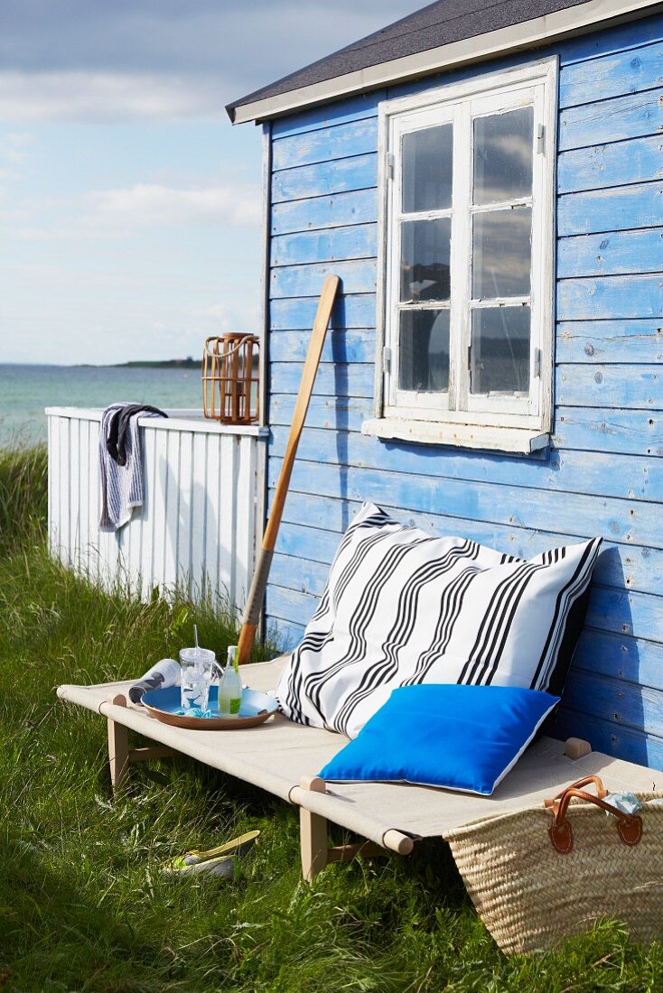 Feldbett vor einem blauen Holzhaus am Meer