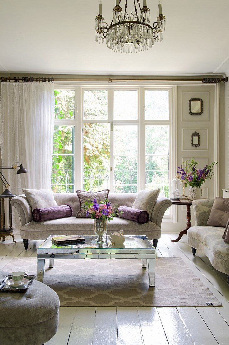 Elegantes Wohnzimmer mit klassischen Polstermöbeln, verspiegeltem Couchtisch und Sprossenfenster