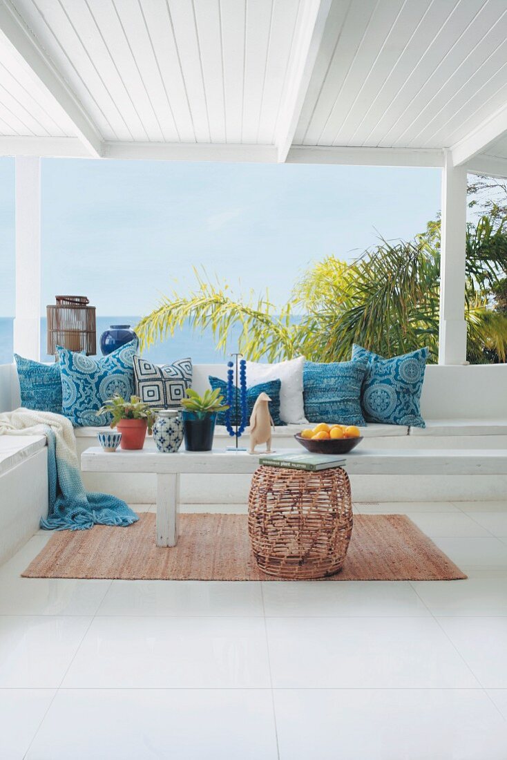 Sitzbank mit verschieden gemusterten blauen Kissen auf sommerlicher Veranda