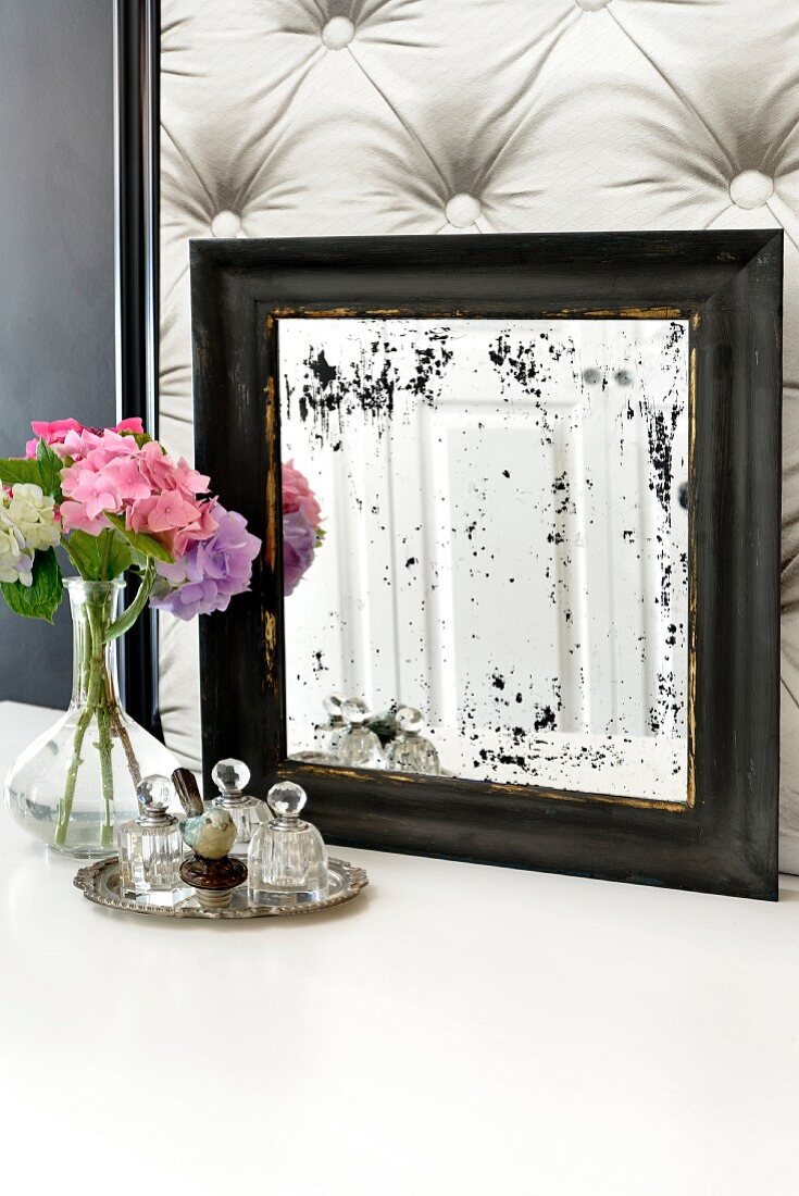 Alter Spiegel mit blinden Flecken, Hortensiensträußchen und kleine Flakons auf Silbertablett