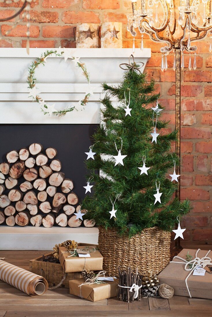 Kleiner Weihnachtsbaum mit Papiersternen und verpackte Geschenke vor einer Kaminkonsole