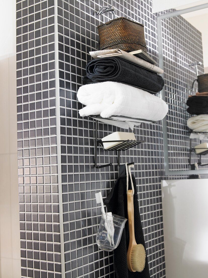Stacked towels on top of wall-mounted shelves with hooks below on grey mosaic-tiled wall
