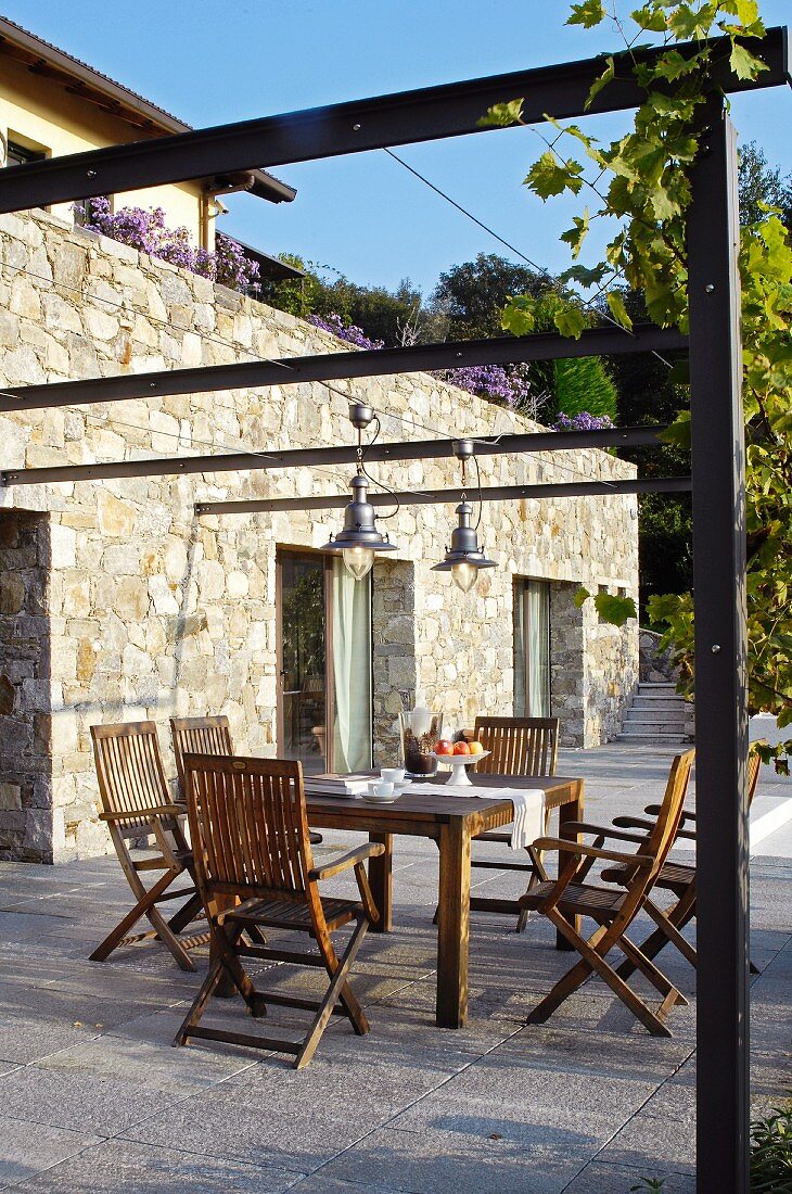 Terrassenplatz mit gedecktem Tisch unter Pergola vor Natursteinfassade und italienischem Flair