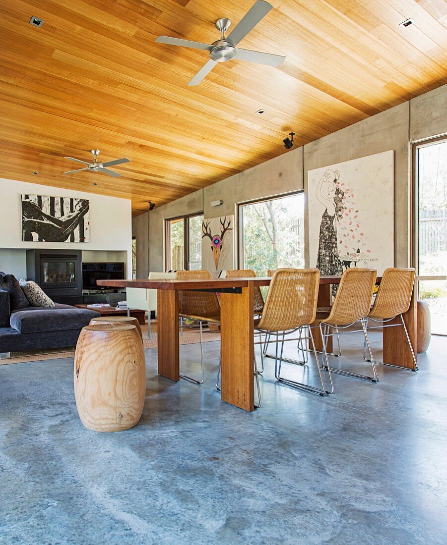 Open living with a solid table, modern wicker chairs, wooden ceiling and pictures