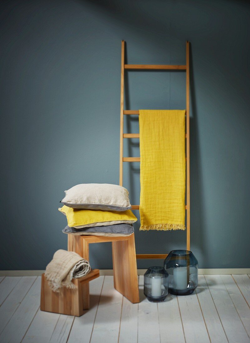 Yellow cloth draped over wooden ladder used as rack and stack of cushions on wooden stool