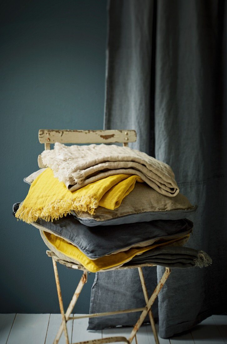 Stack of cushions and cloths in shades of blue and yellow on old garden chair