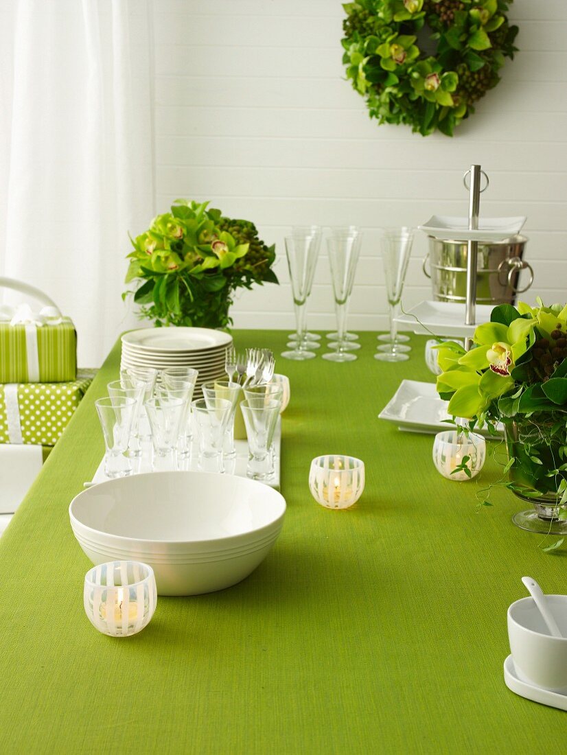 Geschirrstapel, Gläser und Windlichter auf grün gedecktem Tisch mit Blumendekoration