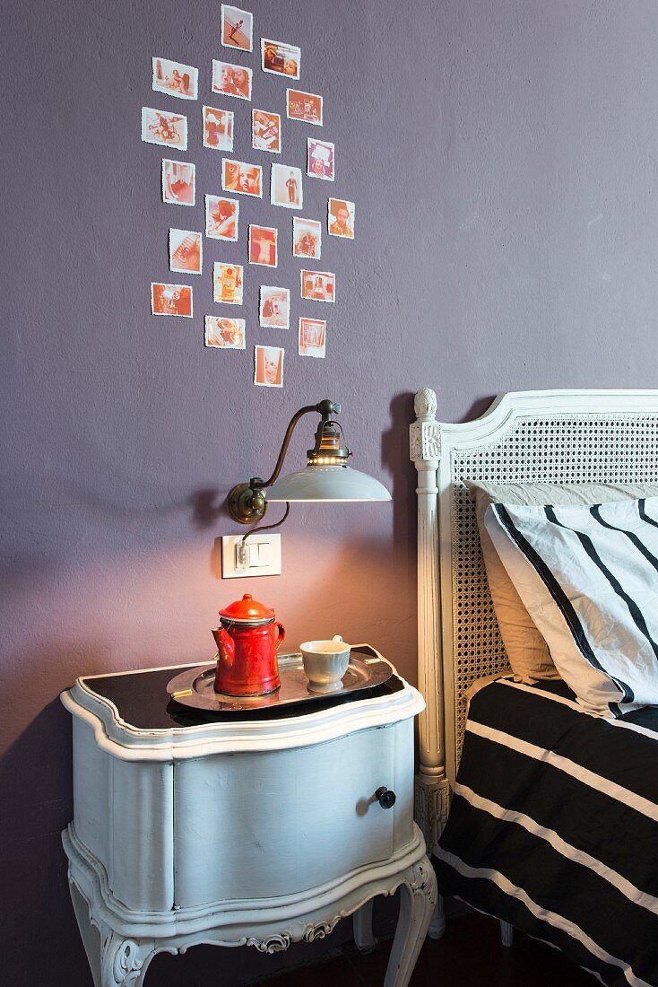 Antikes Nachtkästchen und Vintage Wandleuchte an mauvefarbener Wand mit Fotos im Schlafzimmer