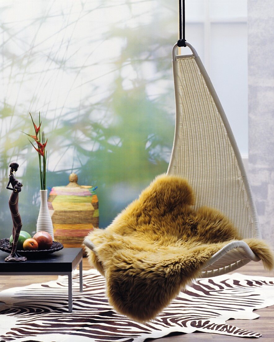 Fur blanket on hanging chair above zebra-skin rug amongst ethnic accessories