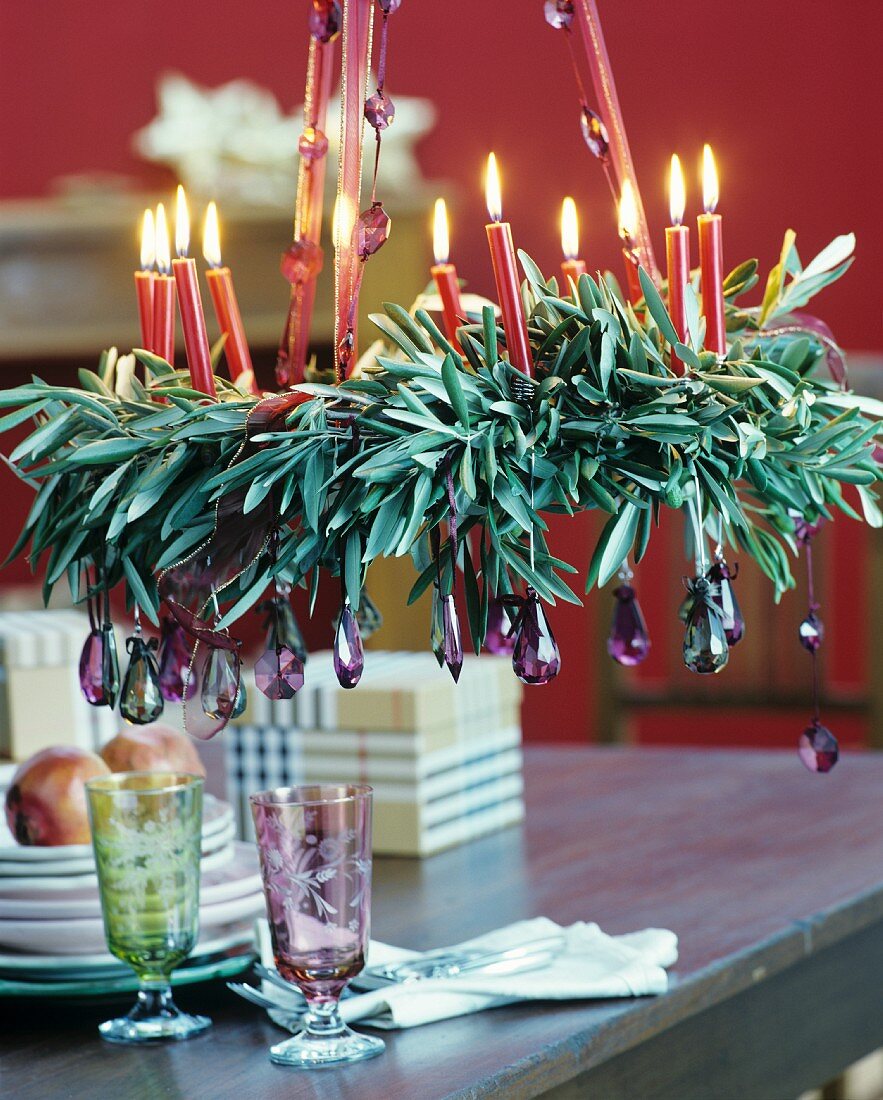 Aufgehängter, weihnachtlicher Kranz aus Olivenzweigen mit brennenden roten Kerzen und lilafarbenen Kristallanhängern