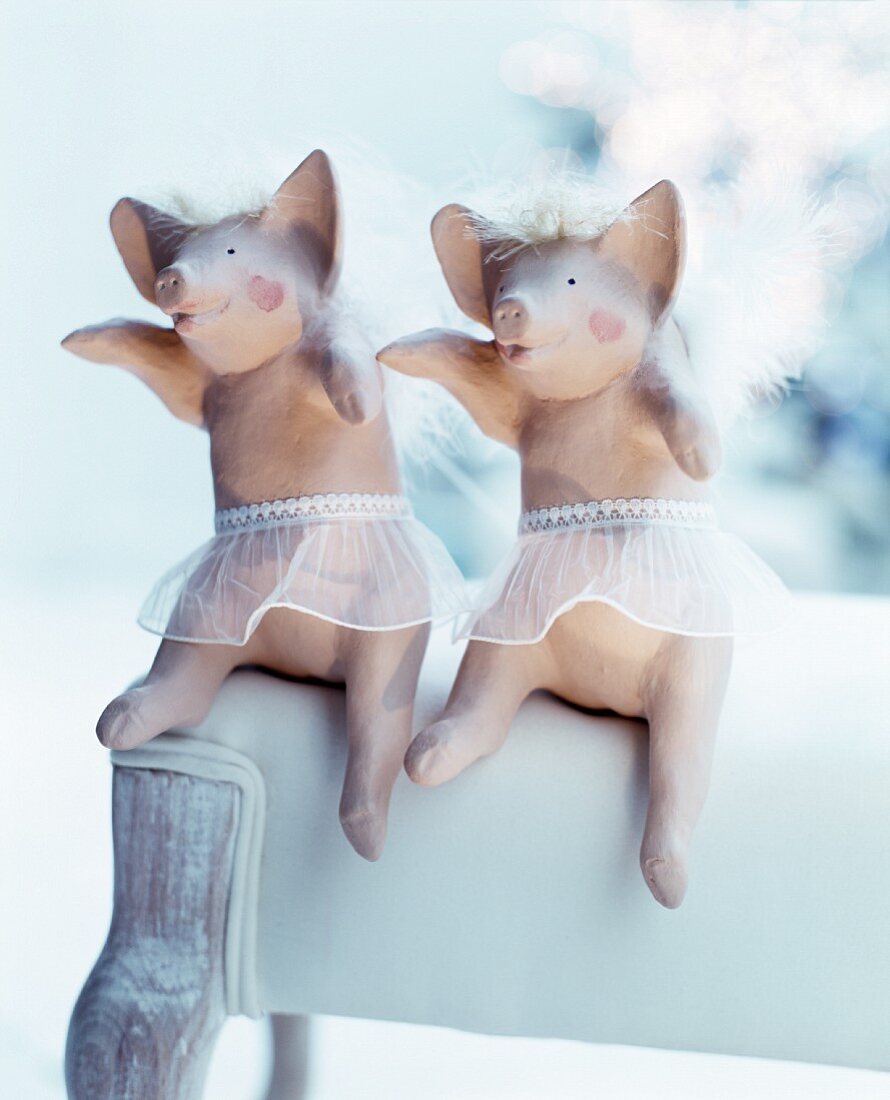 Two angel-pig ornaments arranged on white upholstered chair