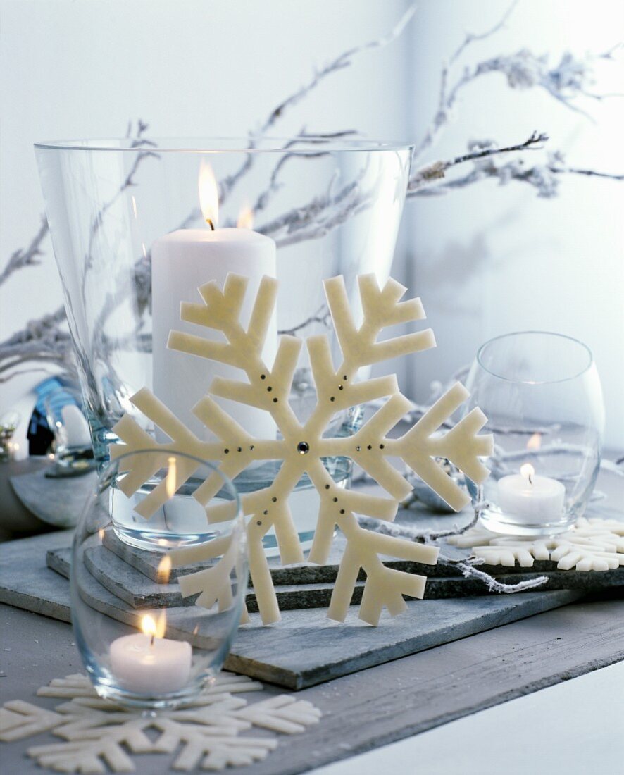 Weihnachtsdekoration mit weißen Kerzen in verschiedenen Glasgefäßen und Deko in Schneeflockenmotiv
