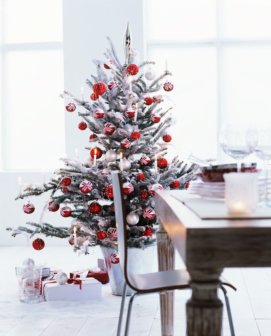 Rotweiss geschmückter Weihnachtsbaum mit brennenden Christbaumkerzen, darunter Weihnachtsgeschenke