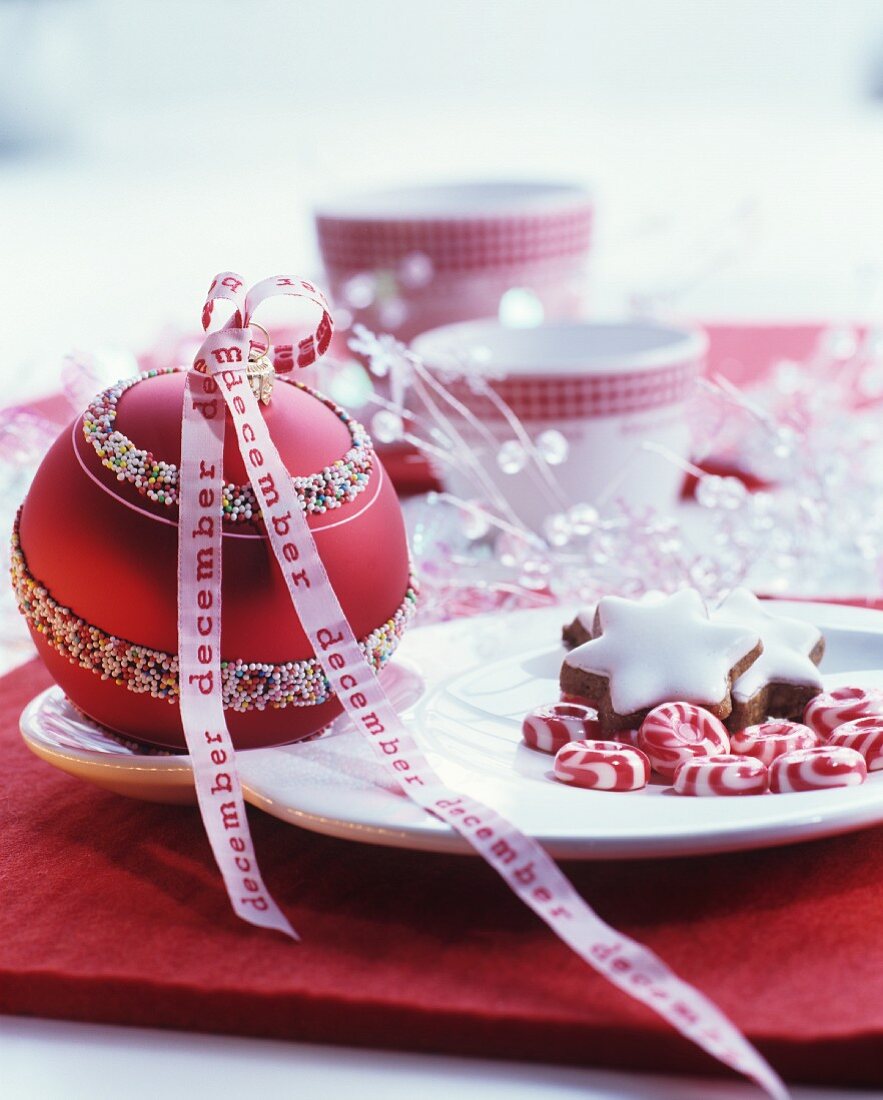 Red bauble with white pattern and white ribbon with red lettering decorating dining table
