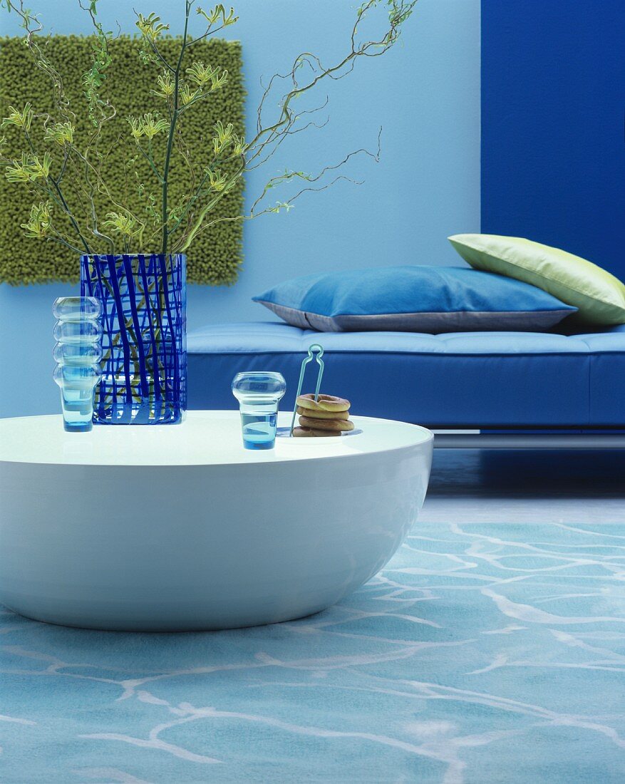 Runder massiver Couchtisch mit blauen Glasvasen vor blauem Sofa