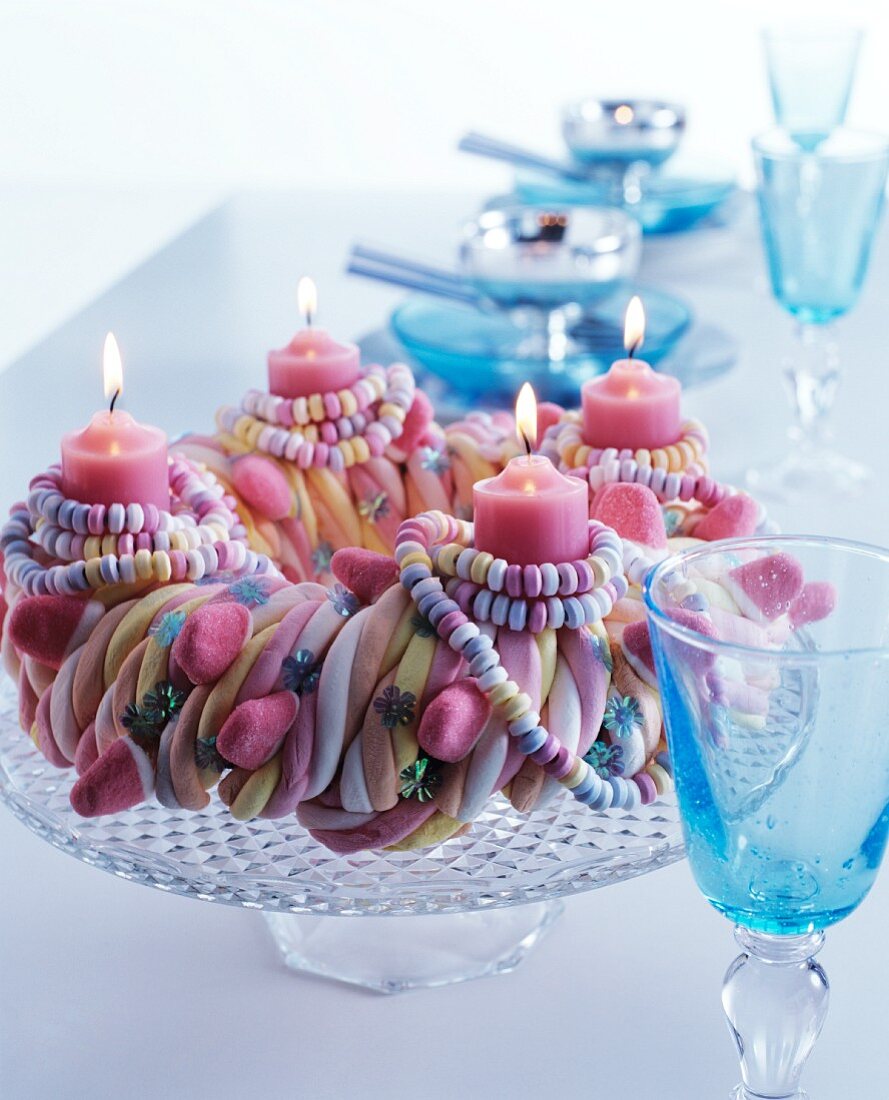 Advent wreath made from sweets with candy necklaces and lit pink candles