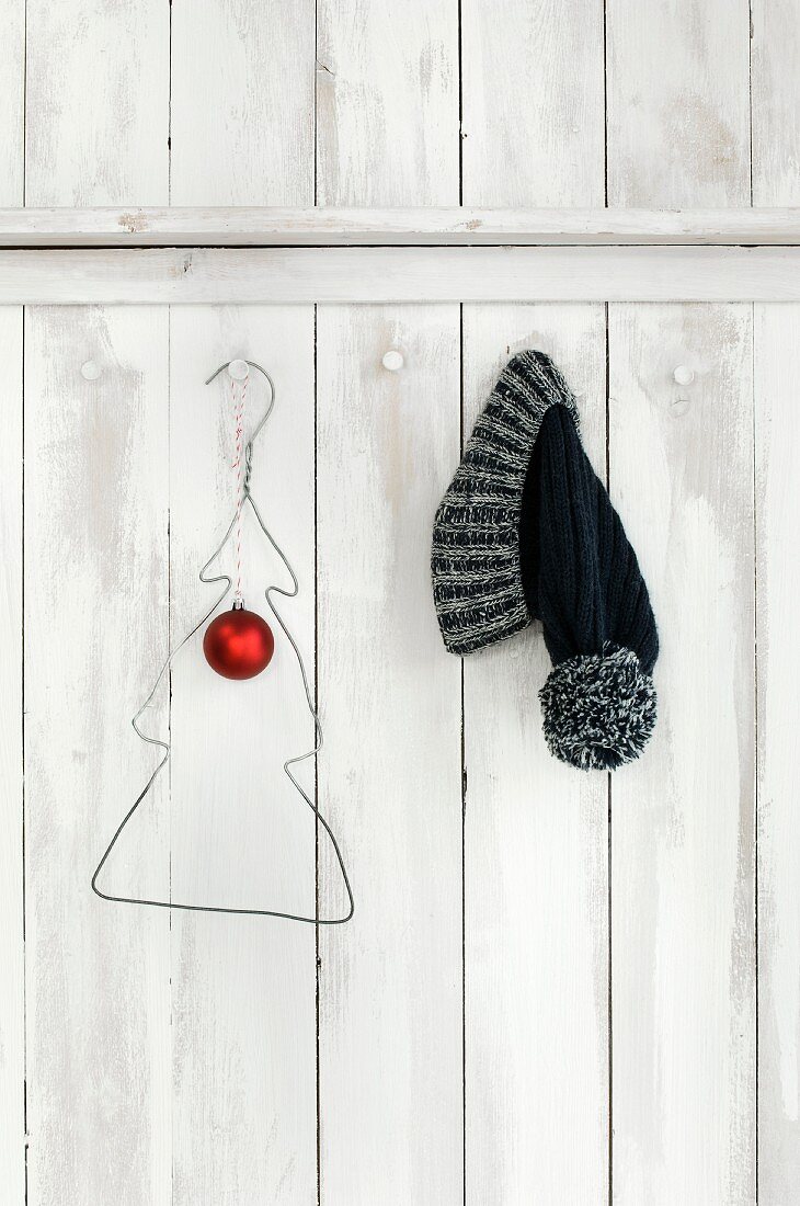 Wire coat hanger bent into Christmas tree shape and bobble hat hung on white-painted board wall