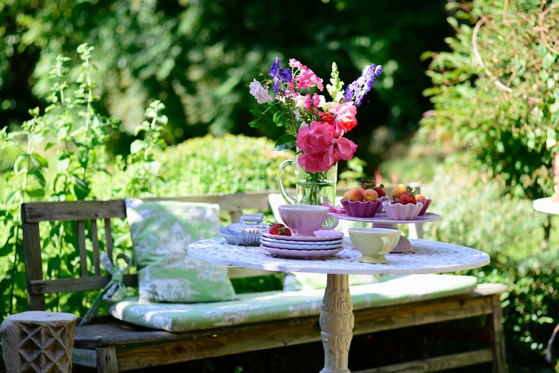 Holzbank und gedeckter Tisch mit Blumenstrauss in sommerlichem Garten