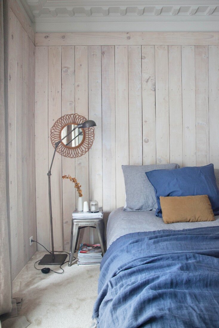 Bed with blue bed linen against white-stained board wall in bedroom