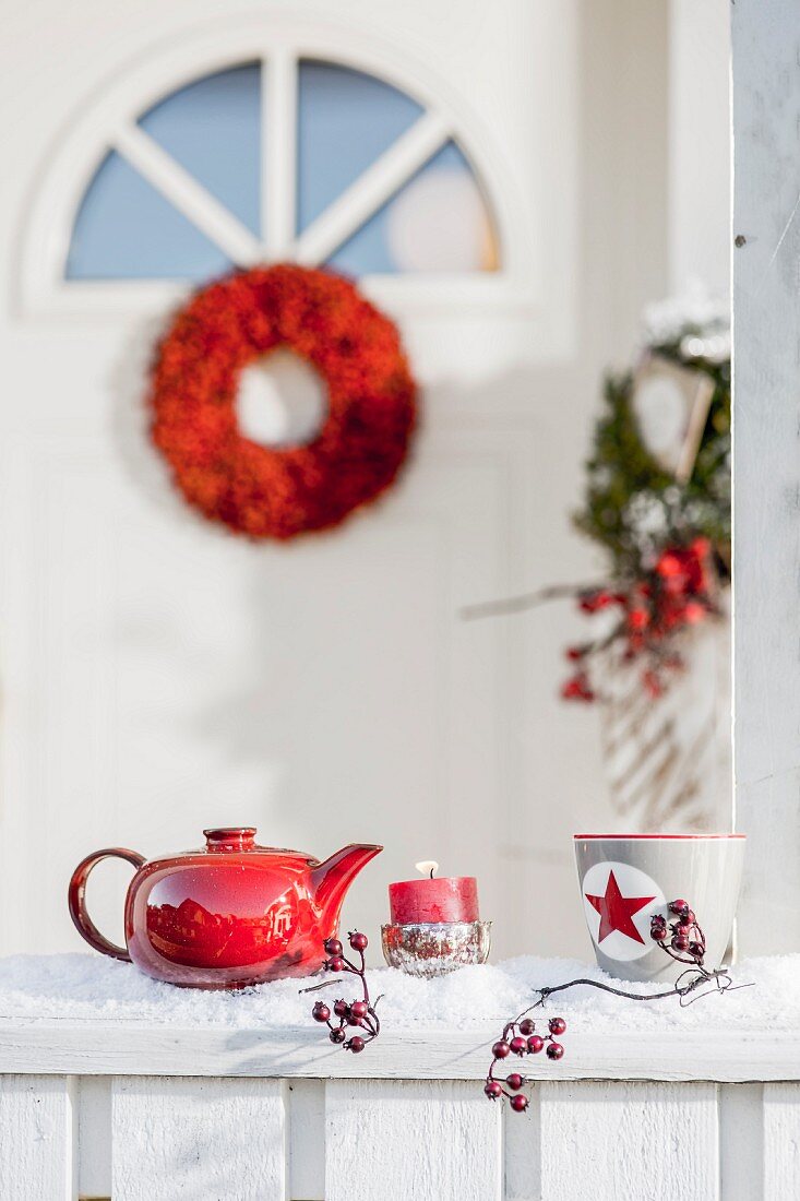 Teekanne, Kerze und Tasse auf verschneitem Geländer vor der Haustür