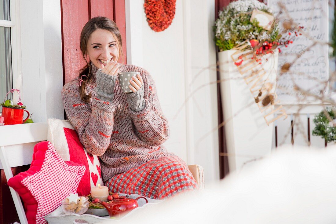 Junge Frau trinkt Kaffee auf der winterlichen Veranda und lacht