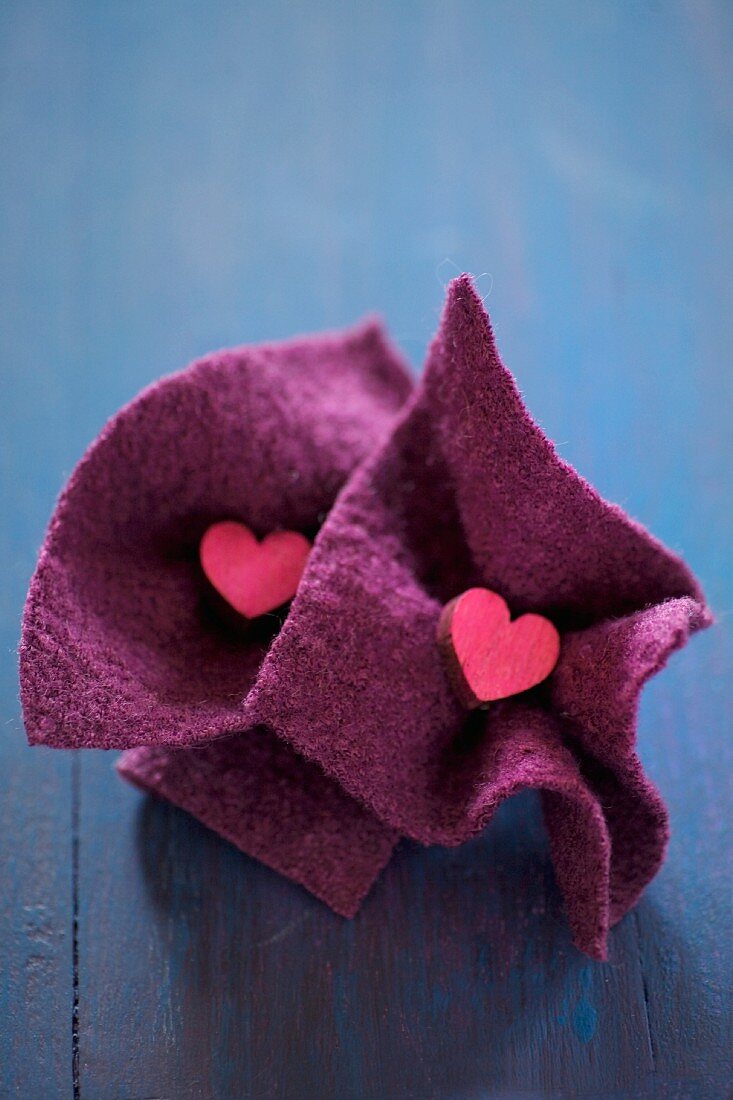 Small wooden hearts in squares of felt on blue surface