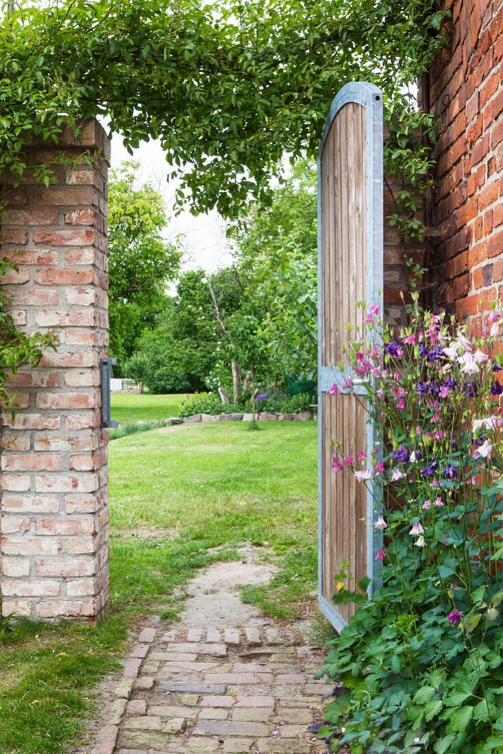 Blick durch Gartentor an Backsteinmauern auf eine Wiese